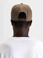 Alpinestars Cappello Acme Snapback, cappello sportswear marrone noce indossato al contrario da un modello, vista posteriore che mostra la chiusura snapback regolabile e l'etichetta con logo sul retro