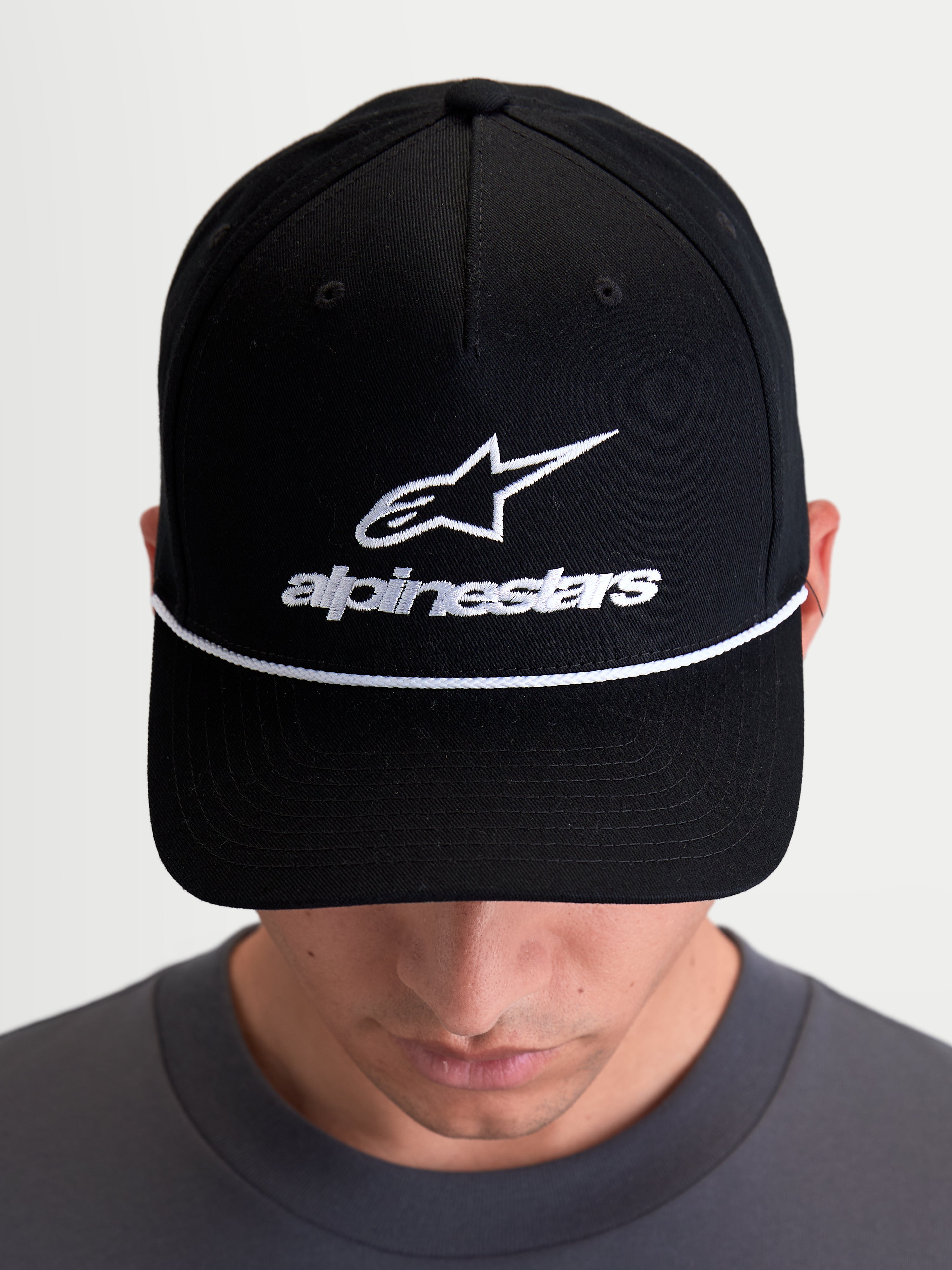 Alpinestars Cappello Combo Logo Snapback, cappello sportswear casual indossato da un modello, nero e bianco, corona strutturata, visiera curva con cordino decorativo bianco e logo Astars ricamato sul davanti