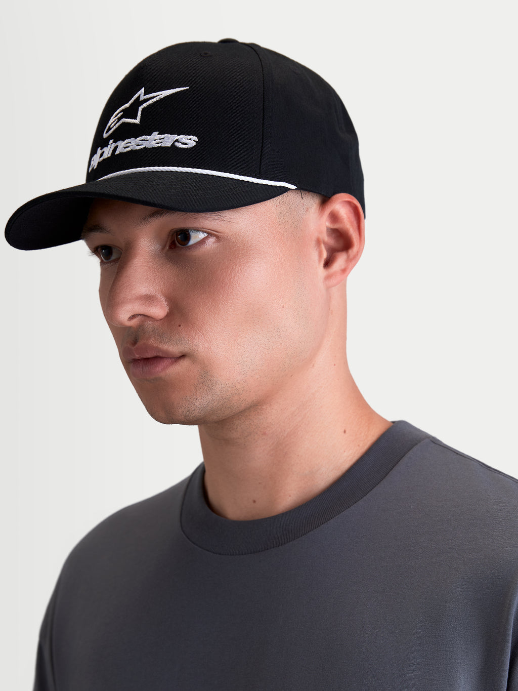 Alpinestars Cappello Combo Logo Snapback, cappello sportswear lifestyle, nero e bianco, visiera curva, corona strutturata con ricamo logo combo Astars bianco e dettaglio cordino, indossato da un modello in vista di profilo.