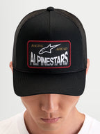 Alpinestars Cappello Hemmings, cappello trucker sportswear indossato da un modello, nero, con pannello frontale in twill, retro in rete traspirante e patch logo frontale