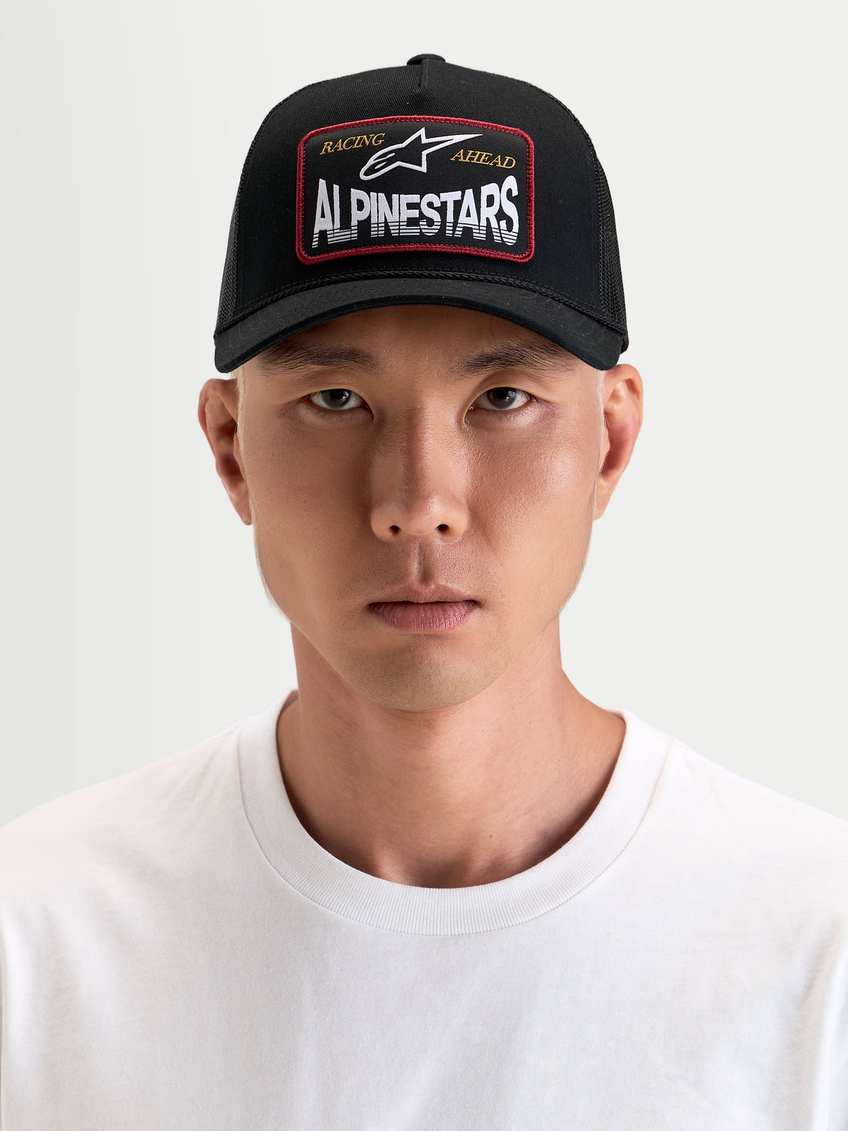 Alpinestars Cappello Hemmings, cappello trucker sportswear nero con visiera curva e patch frontale in tessuto con logo, indossato da un modello