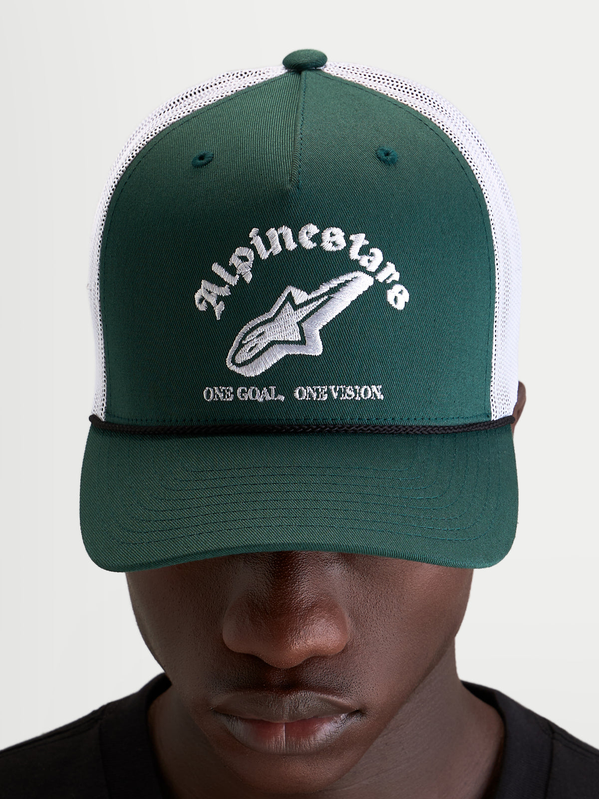 Alpinestars Cappello Baron Trucker, cappellino casual sportswear indossato da un modello, verde e bianco, con visiera curva, frontale strutturato in twill, retro in rete di poliestere traspirante e logo word combo Alpinestars ricamato sul davanti