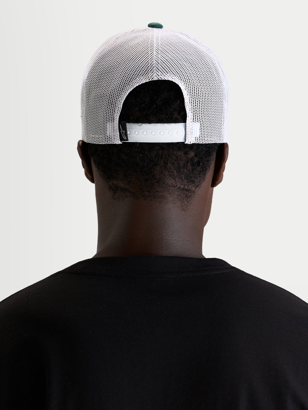 Alpinestars Cappello Baron, cappellino trucker casual sportswear, indossato da un modello, vista posteriore che mostra la chiusura snapback regolabile e pannelli in rete di poliestere bianco con bottone della corona verde