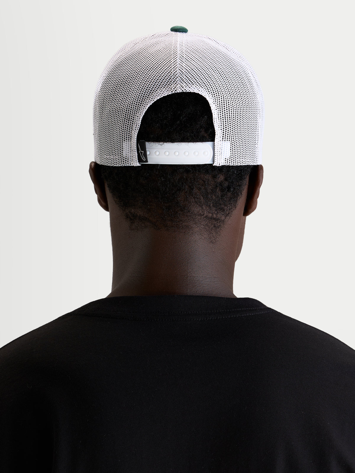Alpinestars Cappello Baron, cappellino trucker casual sportswear, indossato da un modello, vista posteriore che mostra la chiusura snapback regolabile e pannelli in rete di poliestere bianco con bottone della corona verde