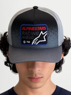 Alpinestars Cappello Gravel Trucker, cappello trucker sportswear, grigio scuro e nero, visiera curva, corona strutturata, patch frontale tessuta con logo Astars e scritta Racing Ahead, retro in rete traspirante, indossato dal modello vista frontale