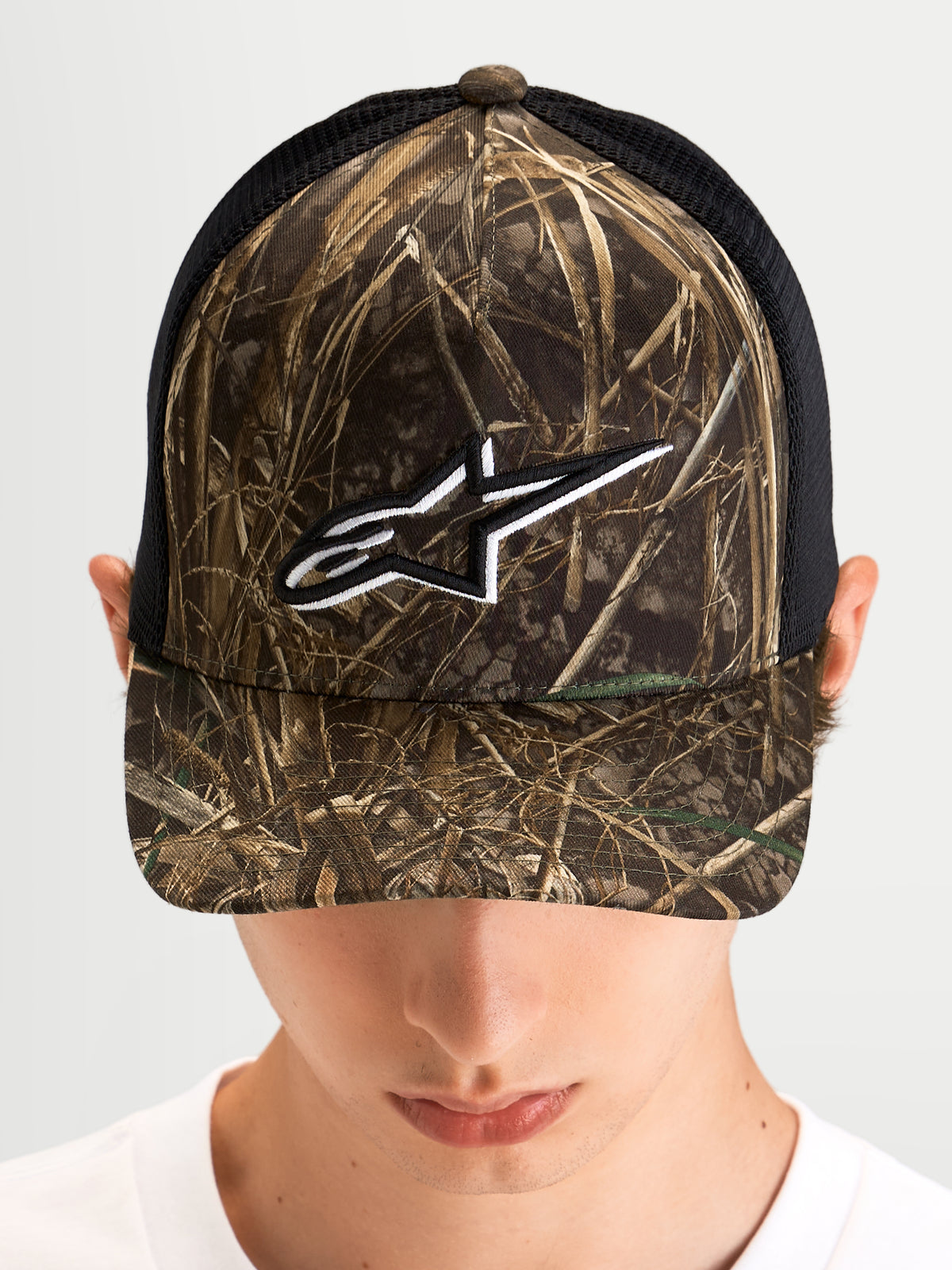Alpinestars Cappello Thicket Realtree Trucker, cappello trucker sportswear indossato da un modello, mimetico Realtree e nero, visiera curva, corona strutturata e logo Astars ricamato in bianco sul davanti
