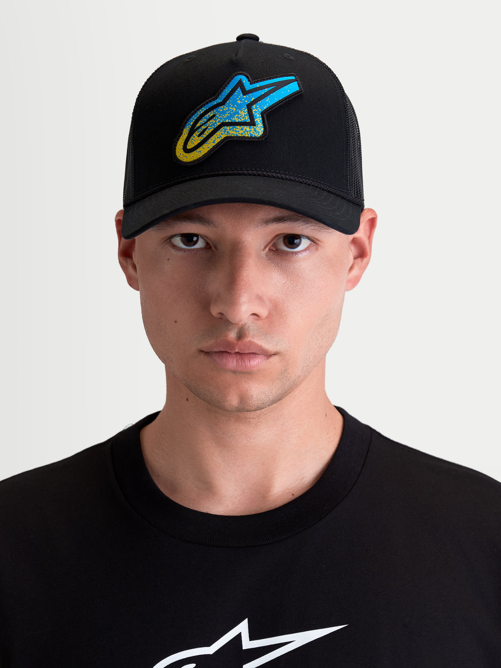 Alpinestars Cappello Meteorite, cappello con visiera curva unisex, nero con patch logo Astars blu e giallo a trama ghiaia, frontale in twill e retro in rete di poliestere, vista frontale su modello