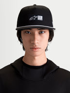 Alpinestars cappello Label Snapback, cappello sportswear nero e bianco, visiera piatta con dettaglio cordino bianco, etichetta frontale tessuta con logo e motto One Goal One Vision, in twill di cotone, indossato da un modello