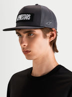 Alpinestars Cappello Ten, cappello trucker sportswear a visiera piatta in grigio scuro, indossato da un modello, con patch frontale con logo Alpinestars ricamato e ricamo laterale del logo Astars