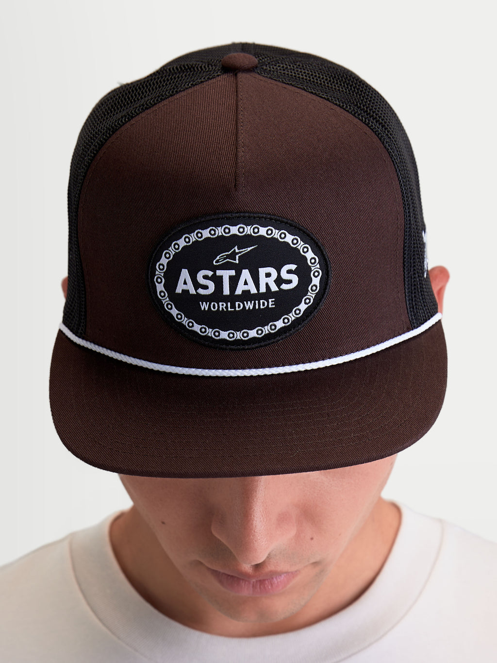 Alpinestars Cappello Hotlink, cappello trucker sportswear su modello, marrone e nero, corona strutturata, visiera piatta con cordino bianco e patch Astars Worldwide con bordo a catena da bici.