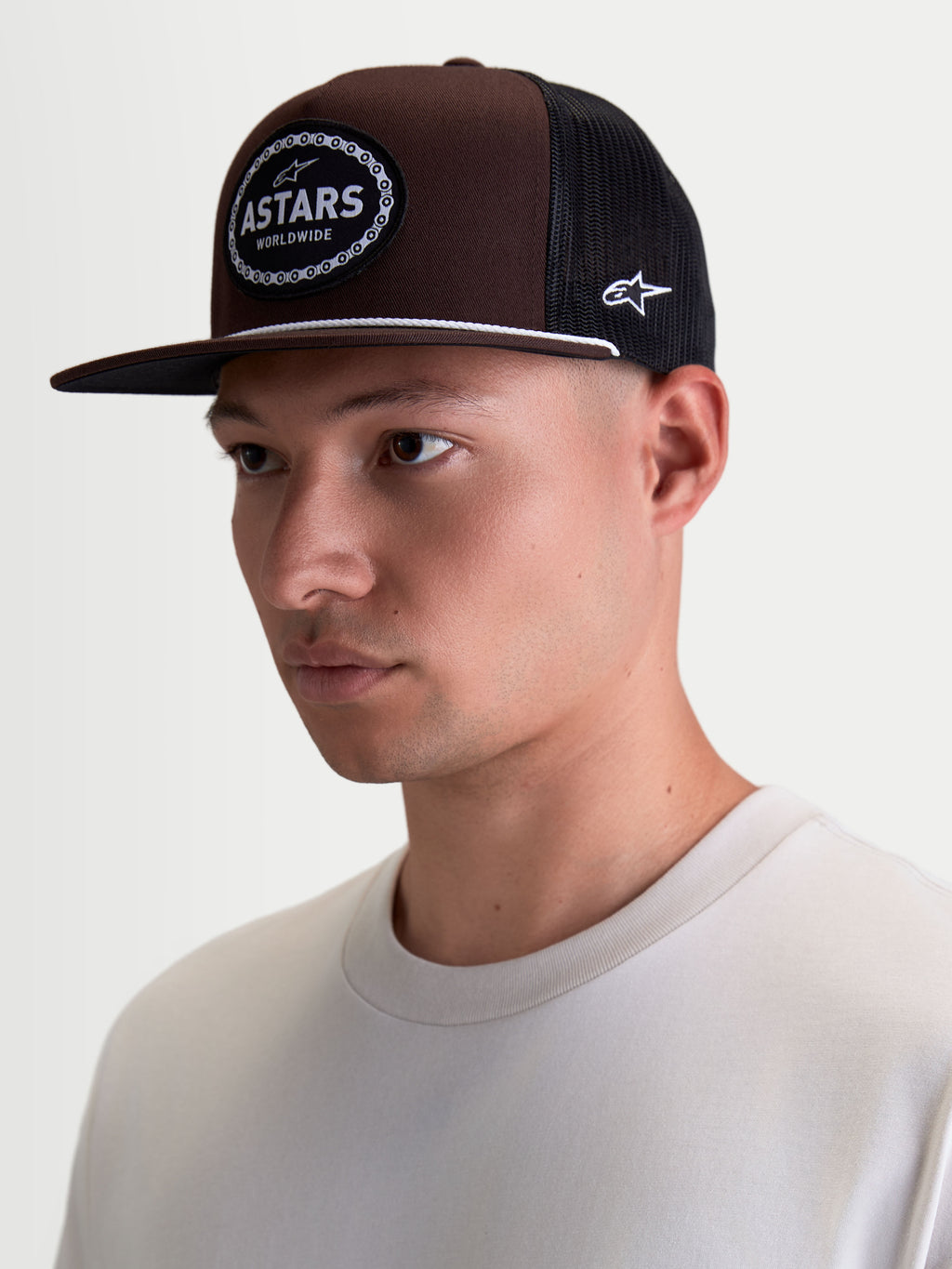 Alpinestars Cappello Hotlink, cappello trucker sportswear, marrone e nero, visiera piatta, corona strutturata in twill, patch frontale Astars con bordo a catena da bici, indossato da un modello