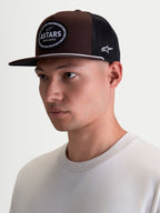 Alpinestars Cappello Hotlink, cappello trucker sportswear, marrone e nero, visiera piatta, corona strutturata in twill, patch frontale Astars con bordo a catena da bici, indossato da un modello