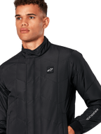 Alpinestars Giacca Precedent, giacca sportiva trapuntata da uomo in nero, primo piano con colletto basso, patch logo sul petto e ricamo sulla manica, caratterizzata da un iconico motivo trapuntato angolato per un look ispirato al motorsport