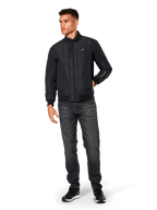 Giacca Alpinestars Precedent, giacca sportswear trapuntata, nera, indossata con jeans grigio scuro e sneakers nere, con motivo trapuntato angolato, colletto basso, polsini e orlo a coste, patch logo bianca sul petto e ricamo sulla manica.