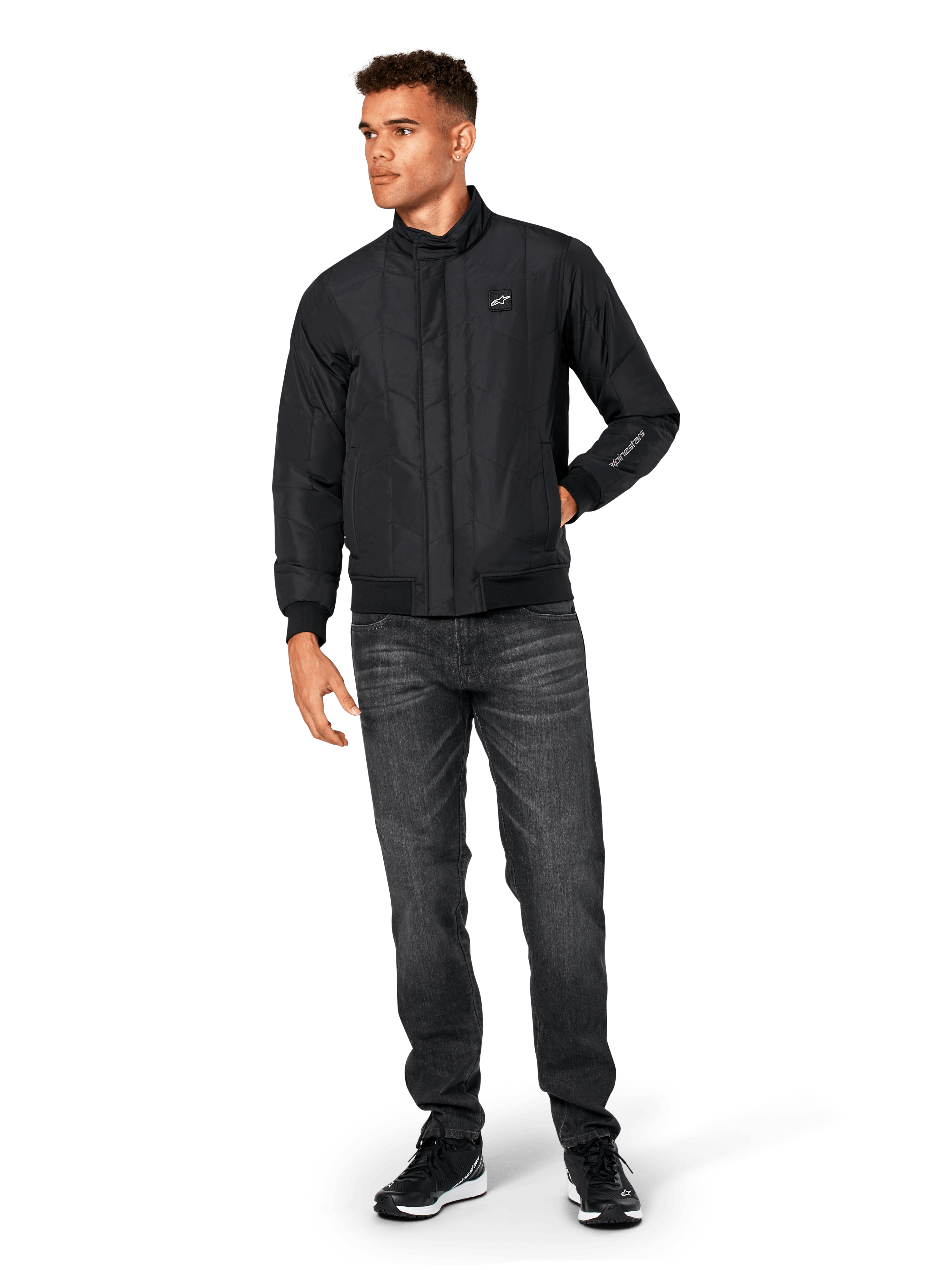 Giacca Alpinestars Precedent, giacca sportswear trapuntata, nera, indossata con jeans grigio scuro e sneakers nere, con motivo trapuntato angolato, colletto basso, polsini e orlo a coste, patch logo bianca sul petto e ricamo sulla manica.