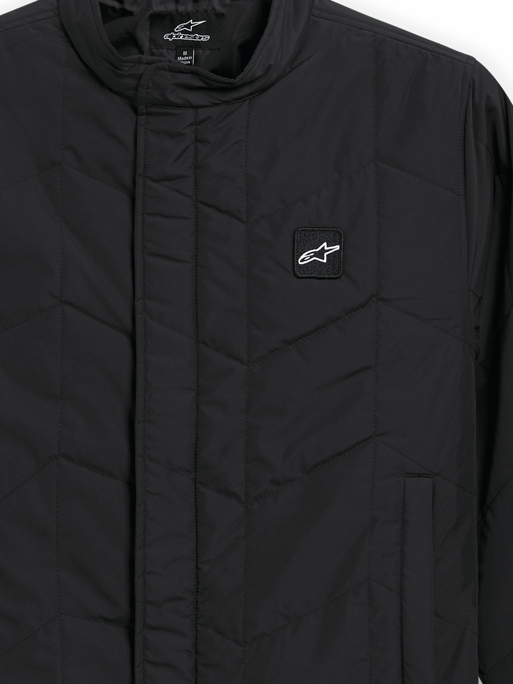 Alpinestars Precedent Jacket, giacca sportswear trapuntata, nero, vista ravvicinata con iconico motivo trapuntato angolato, colletto basso, cerniera frontale coperta e piccola patch con logo sul petto