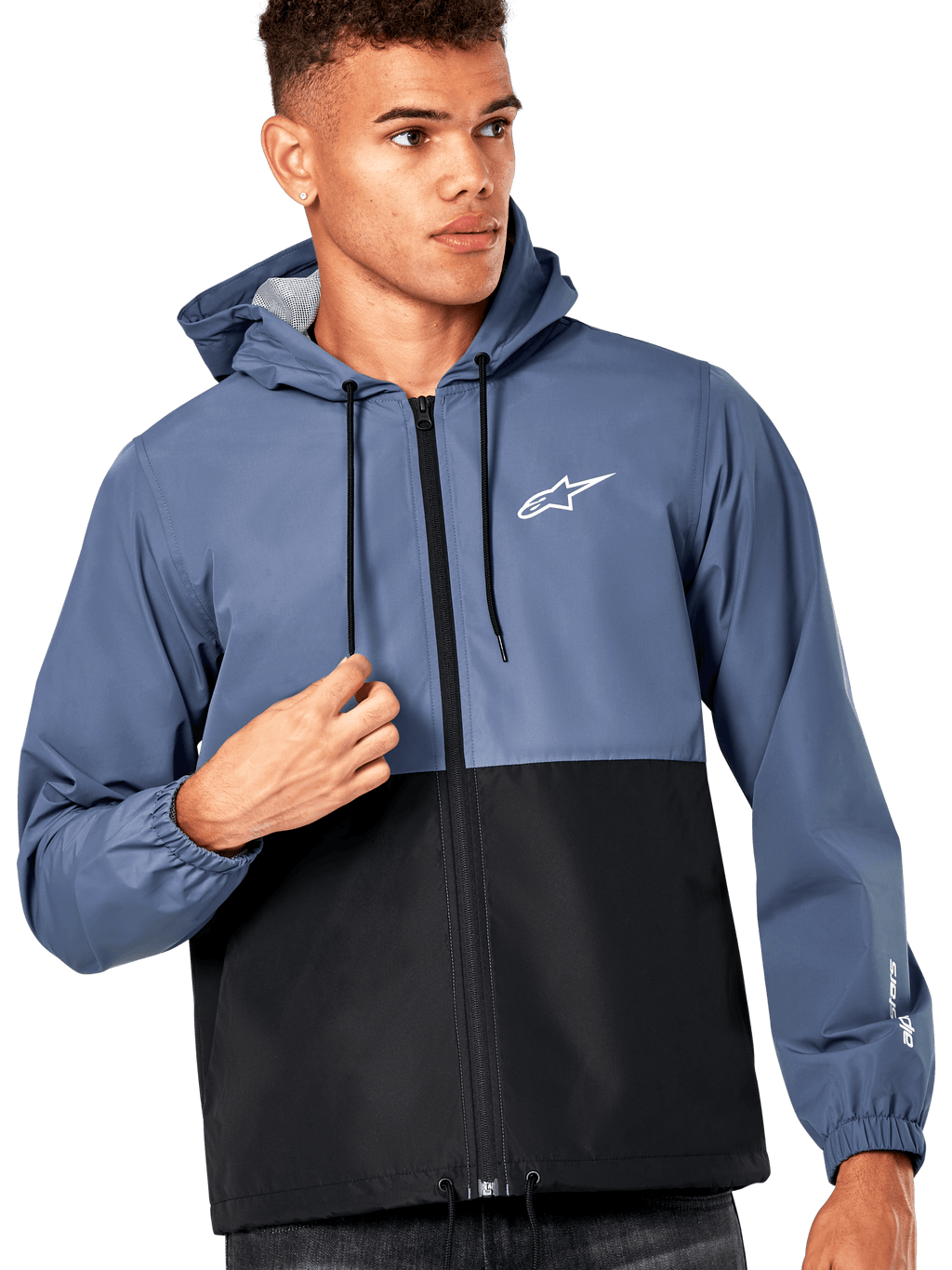Modello uomo che indossa la giacca frangivento Alpinestars Speeder, design a blocchi di colore blu ardesia e nero, con cappuccio e cordini neri, logo bianco sul petto, giacca a vento casual ispirata al motorsport