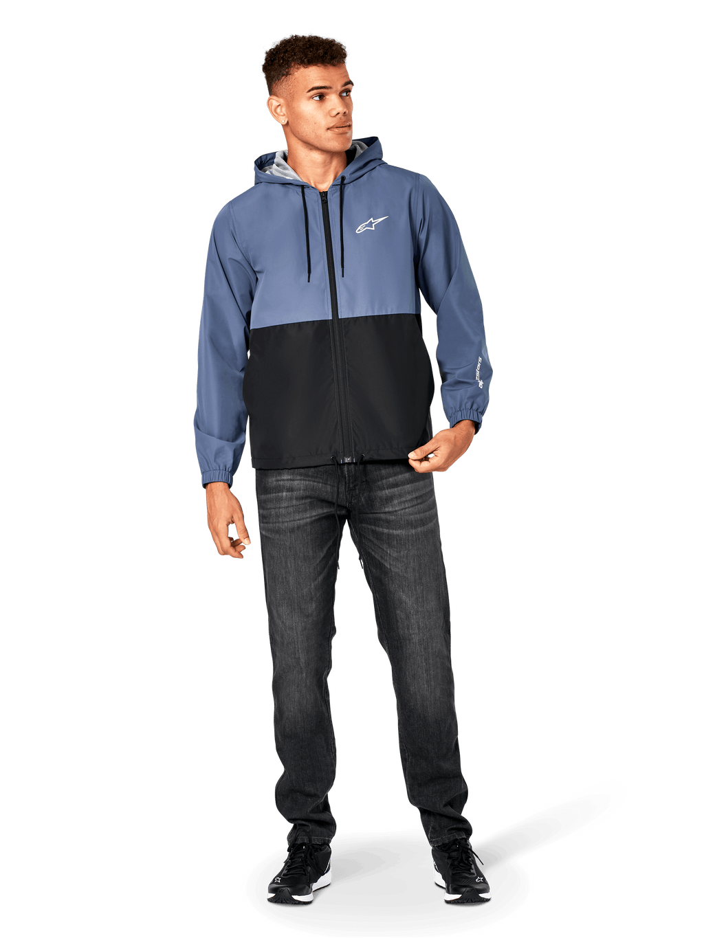 Alpinestars Speeder Windbreaker Jacket, blu ardesia e nero, giacca a vento leggera con cappuccio e fodera in rete, logo con stella bianca sul petto, indossata con jeans neri e sneakers, design casual streetwear motorsport.
