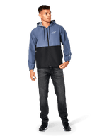 Alpinestars Speeder Windbreaker Jacket, blu ardesia e nero, giacca a vento leggera con cappuccio e fodera in rete, logo con stella bianca sul petto, indossata con jeans neri e sneakers, design casual streetwear motorsport.