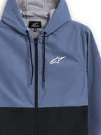 Giacca frangivento Alpinestars Speeder, blu ardesia e nero, giacca a vento leggera con cappuccio, fodera in rete e cordini neri, logo Alpinestars a stella bianco sul petto, design a blocchi di colore, streetwear casual ispirato al motorsport