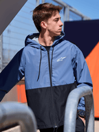 Giacca a vento Alpinestars Speeder, giacca a vento leggera con cappuccio, design color-block blu e nero, logo Alpinestars bianco sul petto, fodera in rete e cappuccio con cordino, streetwear casual ispirato al motorsport
