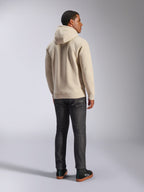 Alpinestars Ageless V3 Hoodie, felpa casual con cappuccio in pile bianco sporco vista dal retro, caratterizzata da polsini e orlo a costine, indossata con jeans scuri slim-fit e sneakers Alpinestars nere