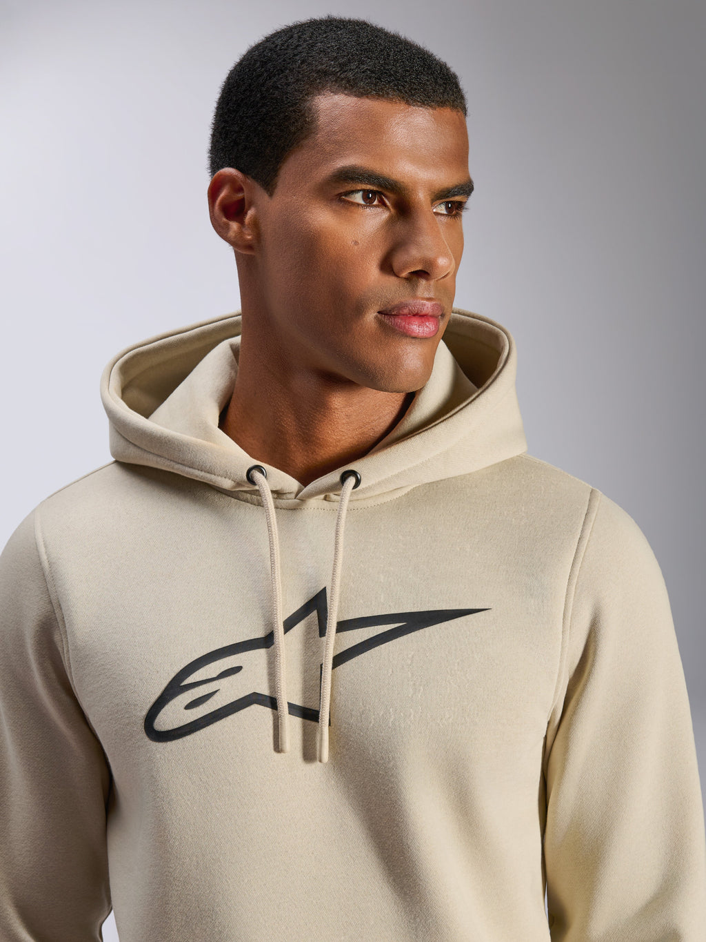 Felpa con cappuccio Alpinestars Ageless V3, abbigliamento sportivo casual, bianco sporco con logo a stella Alpinestars ricamato in nero, cappuccio con cordini, vista ravvicinata su modello, morbido pile, design moderno ispirato al motorsport