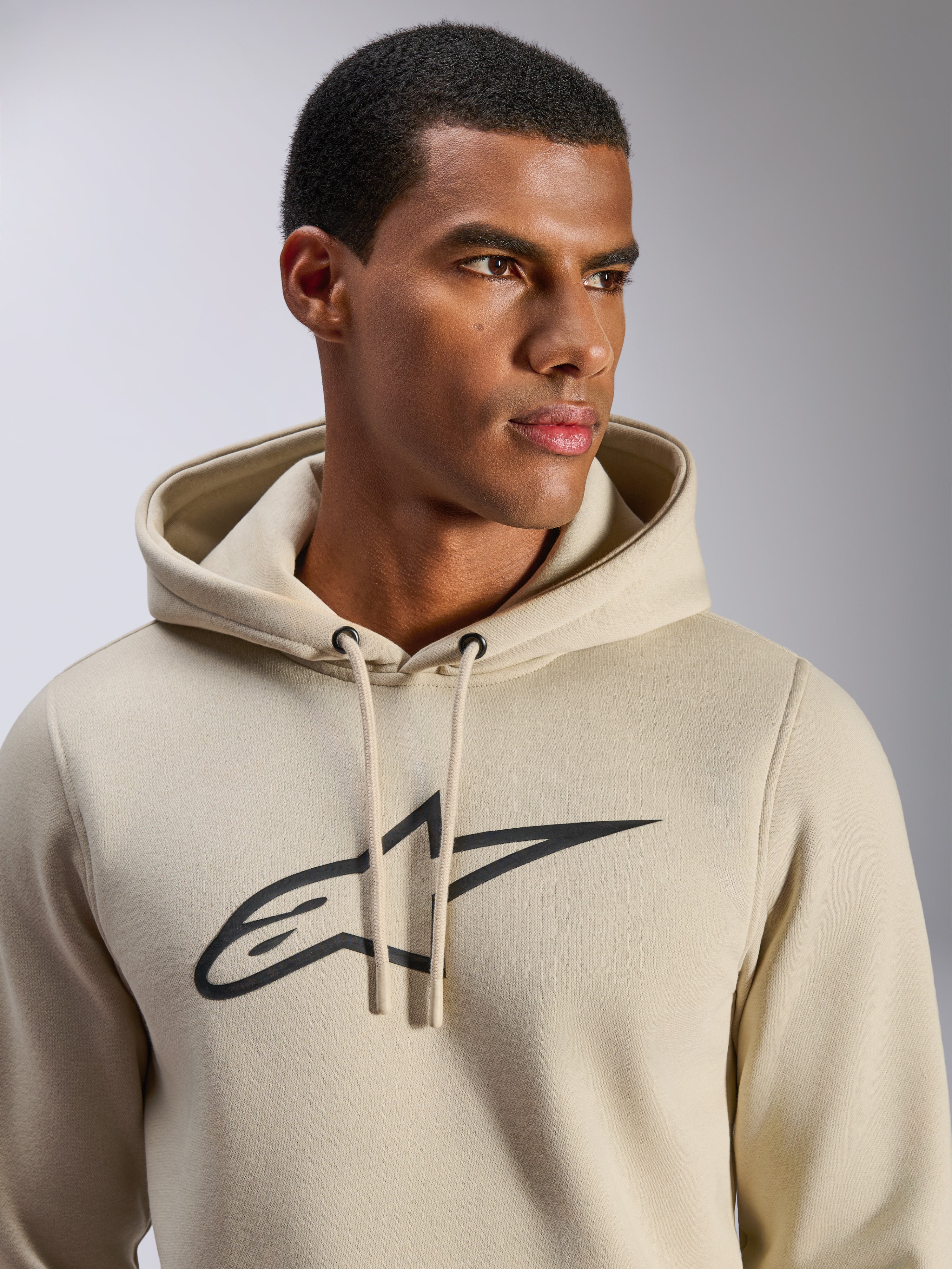 Felpa con cappuccio Alpinestars Ageless V3, abbigliamento sportivo casual, bianco sporco con logo a stella Alpinestars ricamato in nero, cappuccio con cordini, vista ravvicinata su modello, morbido pile, design moderno ispirato al motorsport