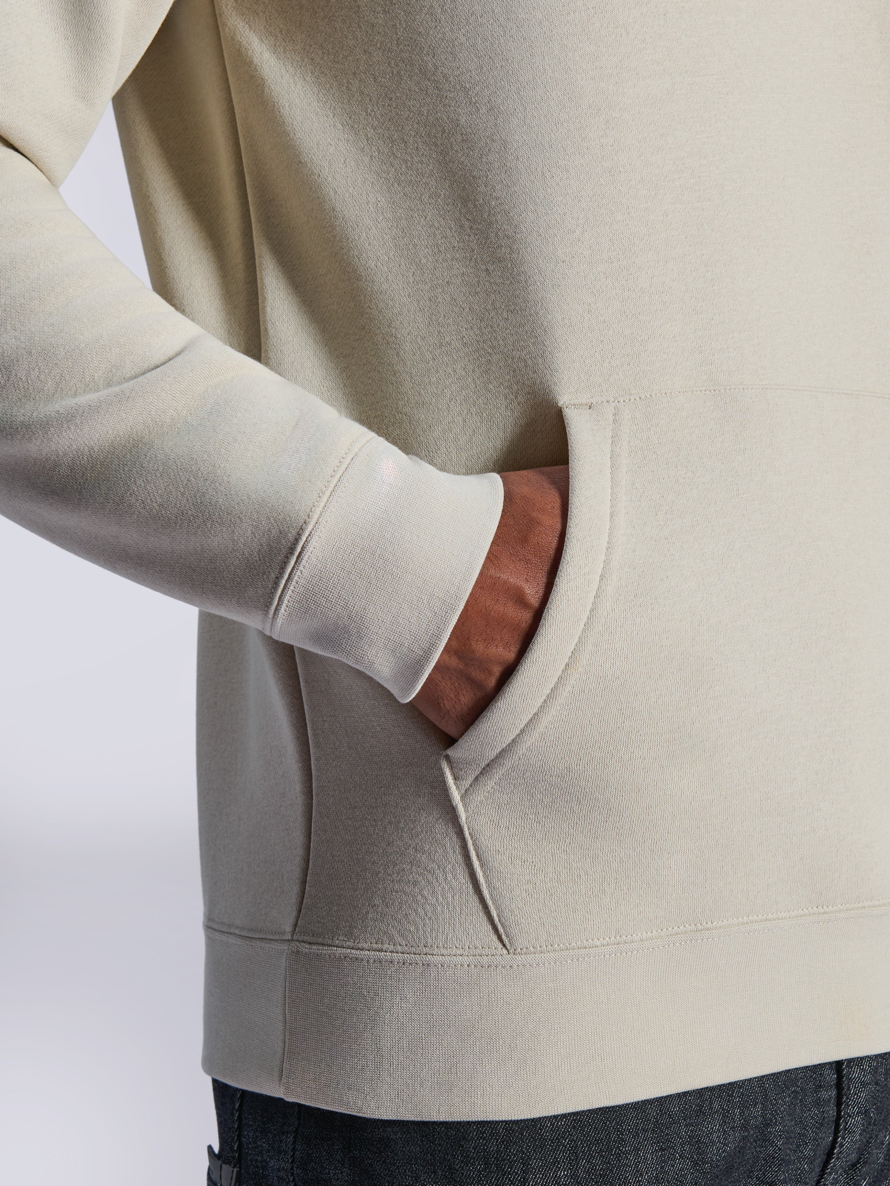 Alpinestars Ageless V3 Hoodie, dettaglio ravvicinato della tasca a marsupio frontale e del polsino a costine, pile bianco sporco, streetwear casual ispirato al motorsport