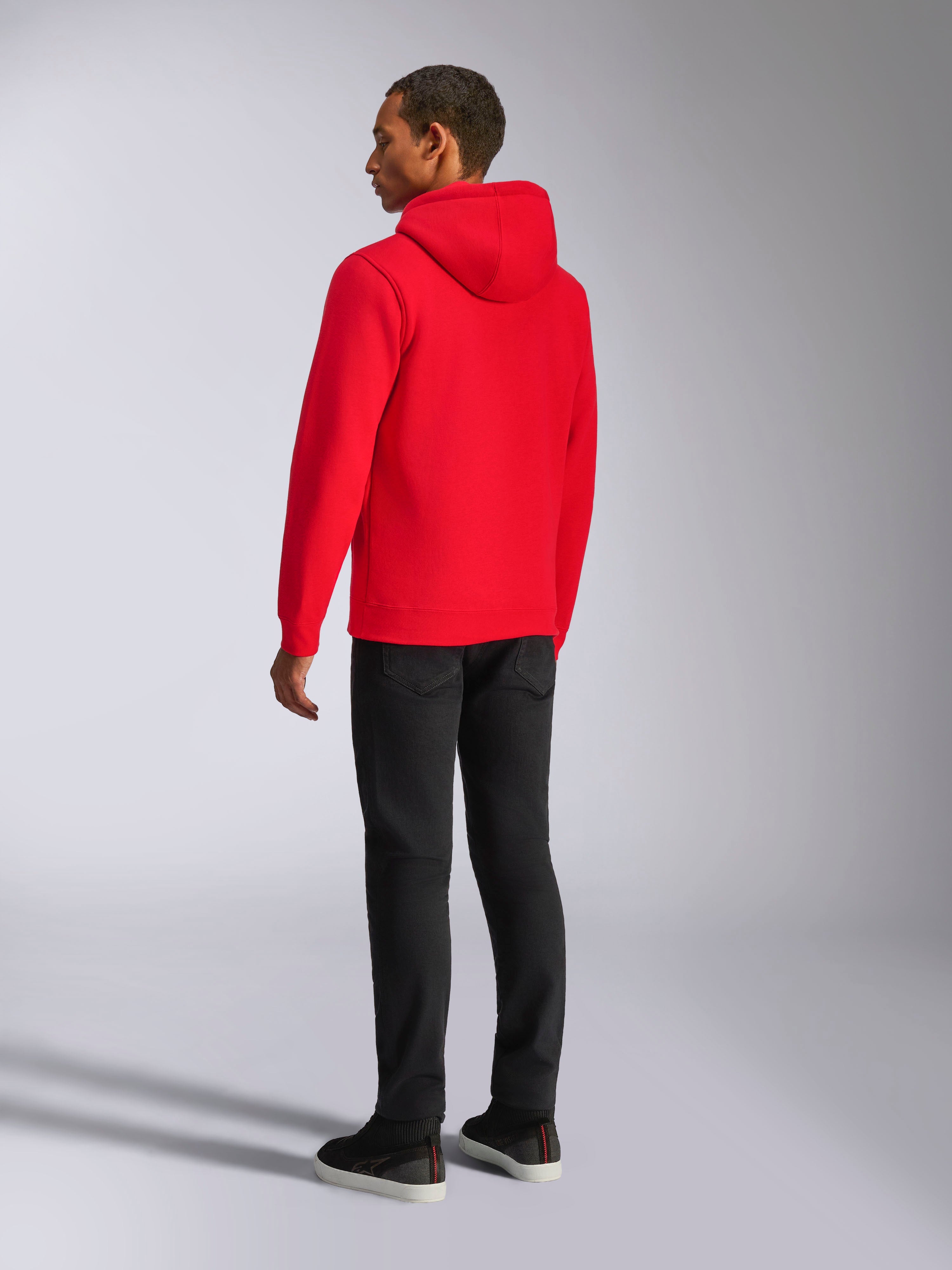 Felpa con cappuccio Alpinestars Ageless V3, streetwear casual, rosso vivace, vista posteriore del modello, con cappuccio foderato in jersey, polsini e orlo a coste, abbinata a pantaloni neri, design moderno ispirato al motorsport