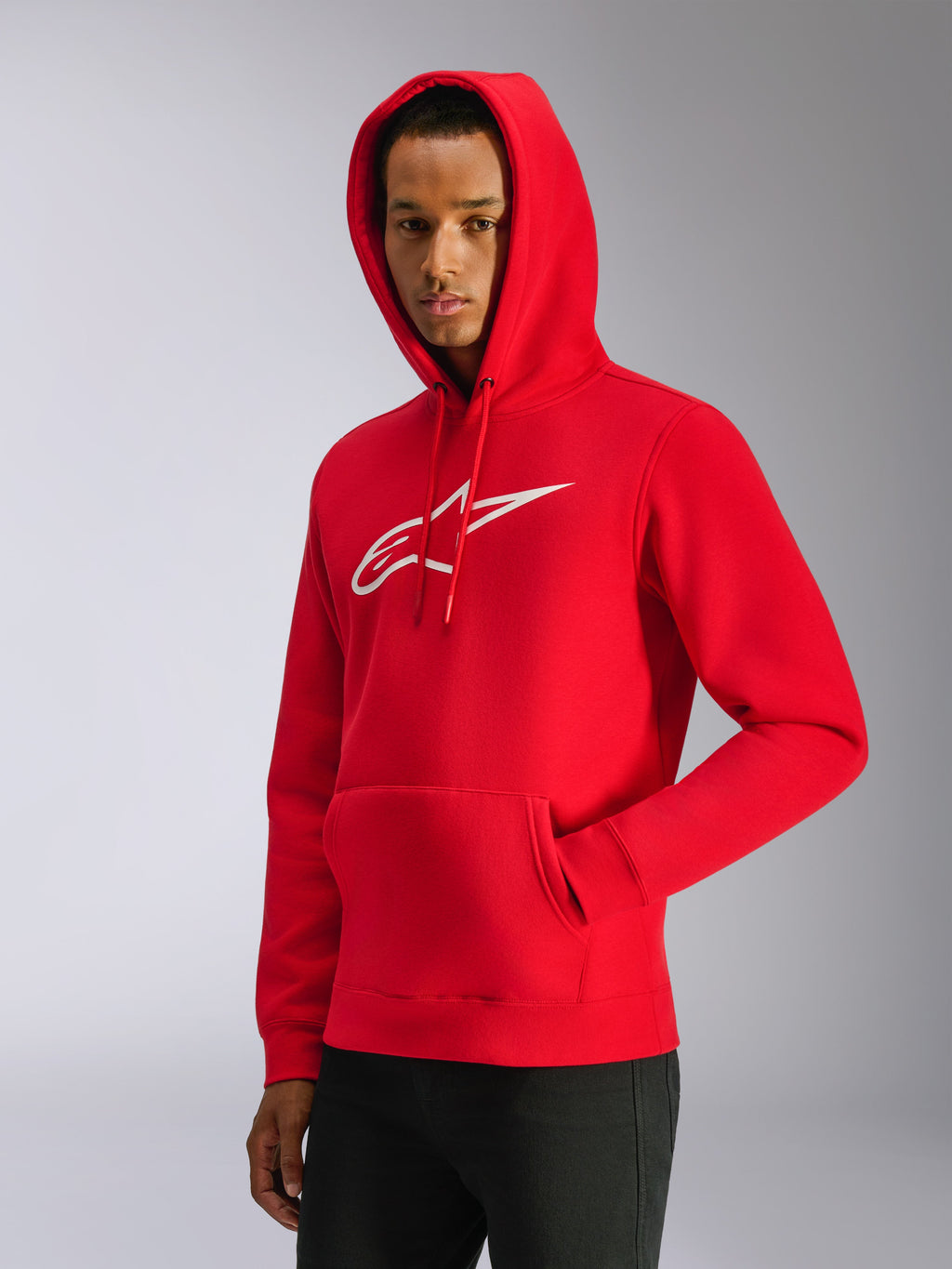 Alpinestars Ageless V3 Hoodie, rossa, modello che indossa la felpa con cappuccio sollevato, logo bianco ricamato sul petto, tasca a marsupio frontale, streetwear casual d'ispirazione motorsport