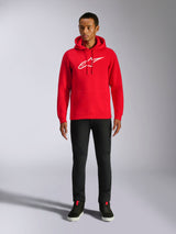 Felpa con cappuccio Alpinestars Ageless V3, streetwear casual, rossa con logo Alpinestars bianco ricamato, indossata da un modello con pantaloni neri, cappuccio con coulisse, tasca a marsupio anteriore, design moderno ispirato al motorsport