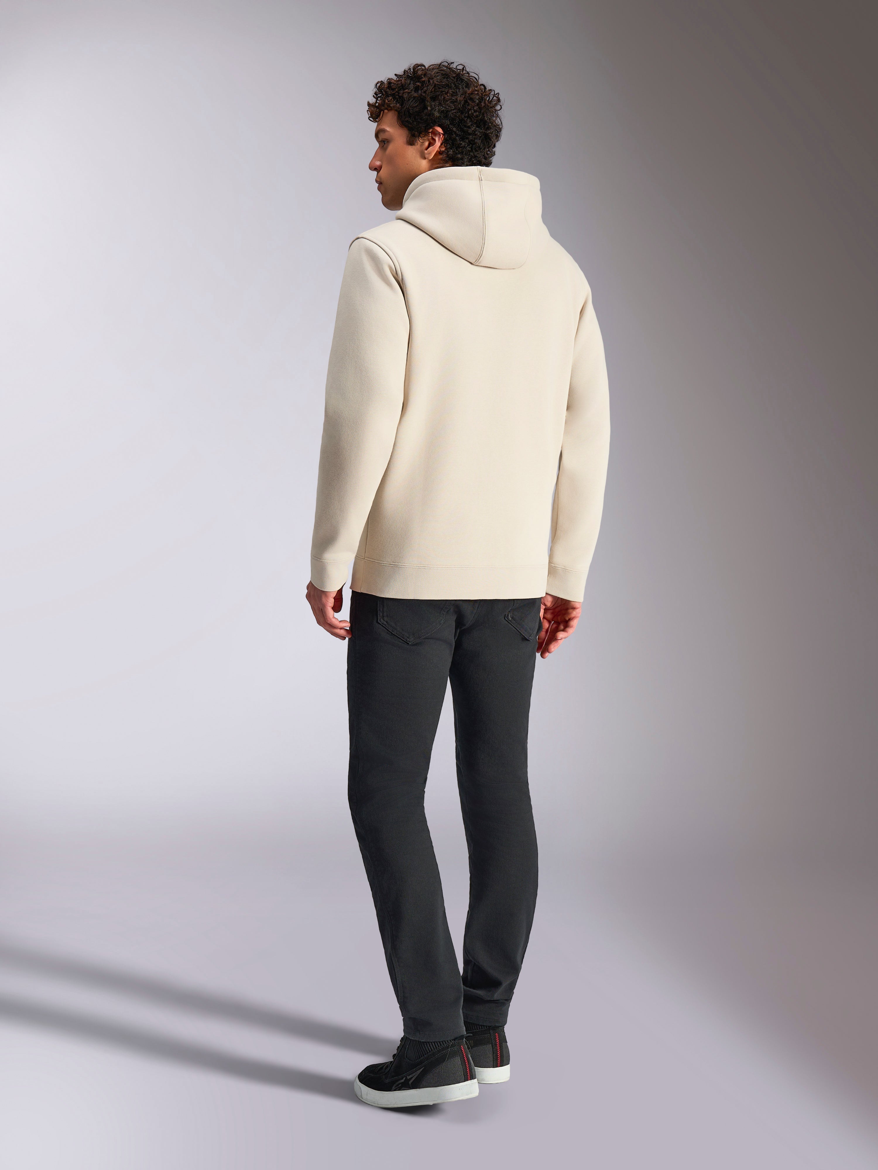 Alpinestars Always V3 Hoodie, bianco sporco, vista posteriore di un modello maschile che indossa la felpa e pantaloni neri, streetwear casual ispirato al motorsport, design minimalista con cappuccio e orlo a costine