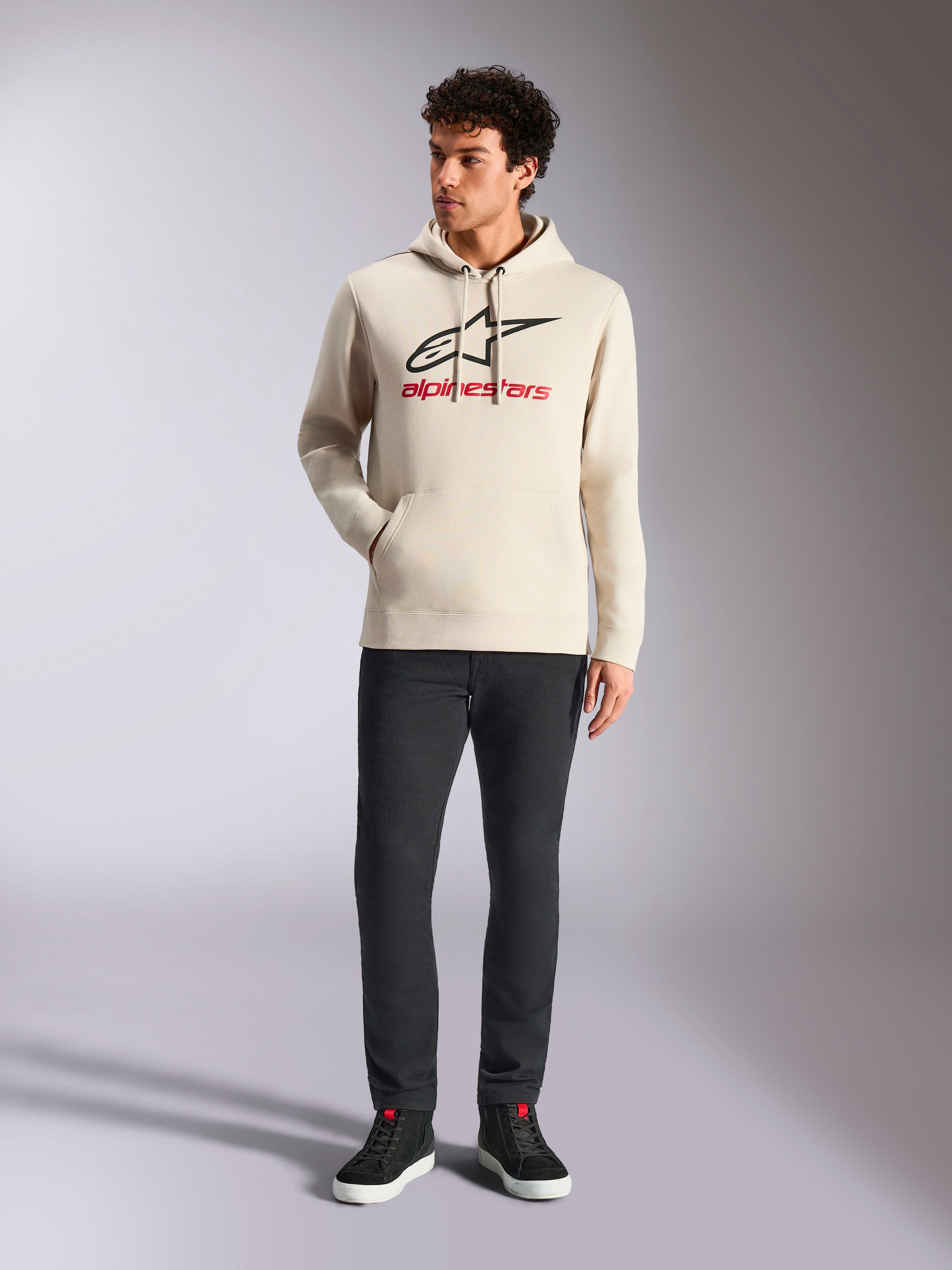 Alpinestars Always V3 Hoodie, streetwear casual, bianco sporco con logo a stella nero e scritte rosse, cappuccio con coulisse, maniche lunghe, indossata da modello uomo con pantaloni neri e sneaker nere