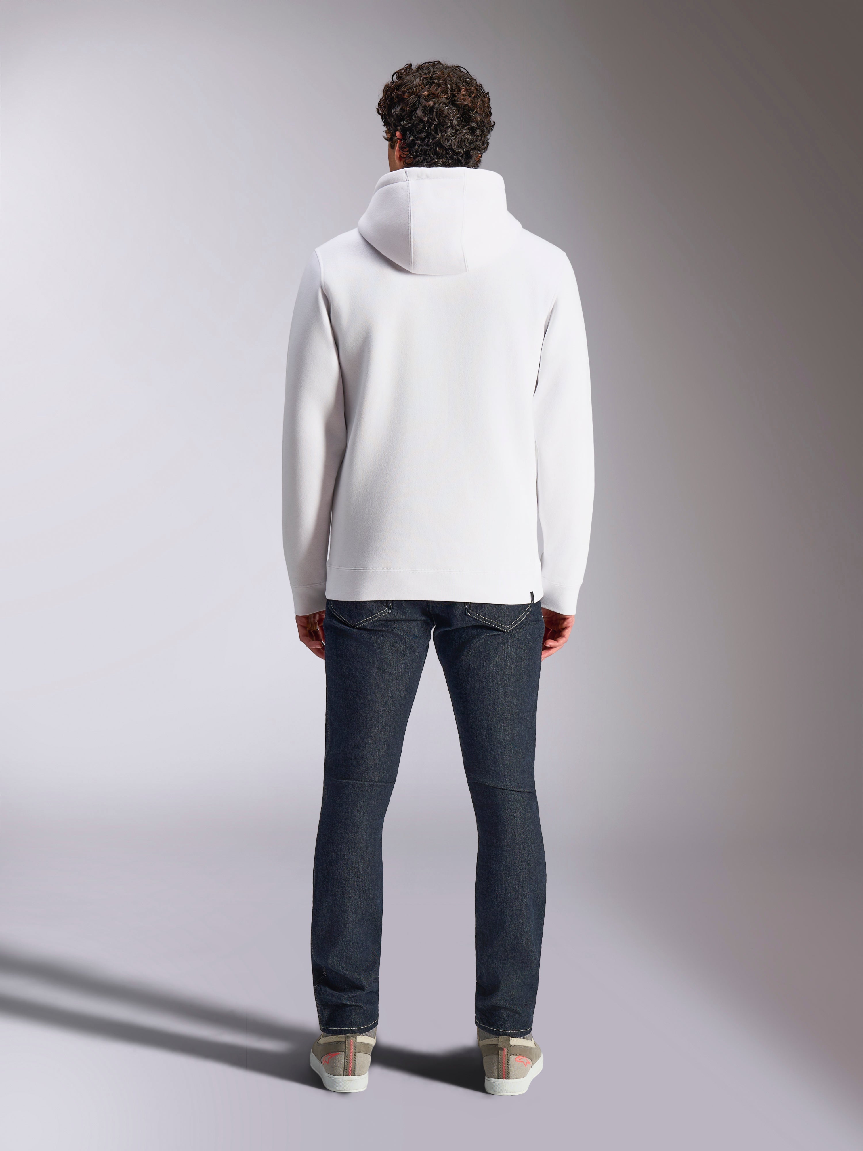 Alpinestars Blaze V3 Hoodie, felpa casual sportiva bianca, vista posteriore della felpa in pile, design pulito con polsini e orlo a costine, abbinata a jeans blu scuro e sneakers, abbigliamento lifestyle moderno ispirato al motorsport