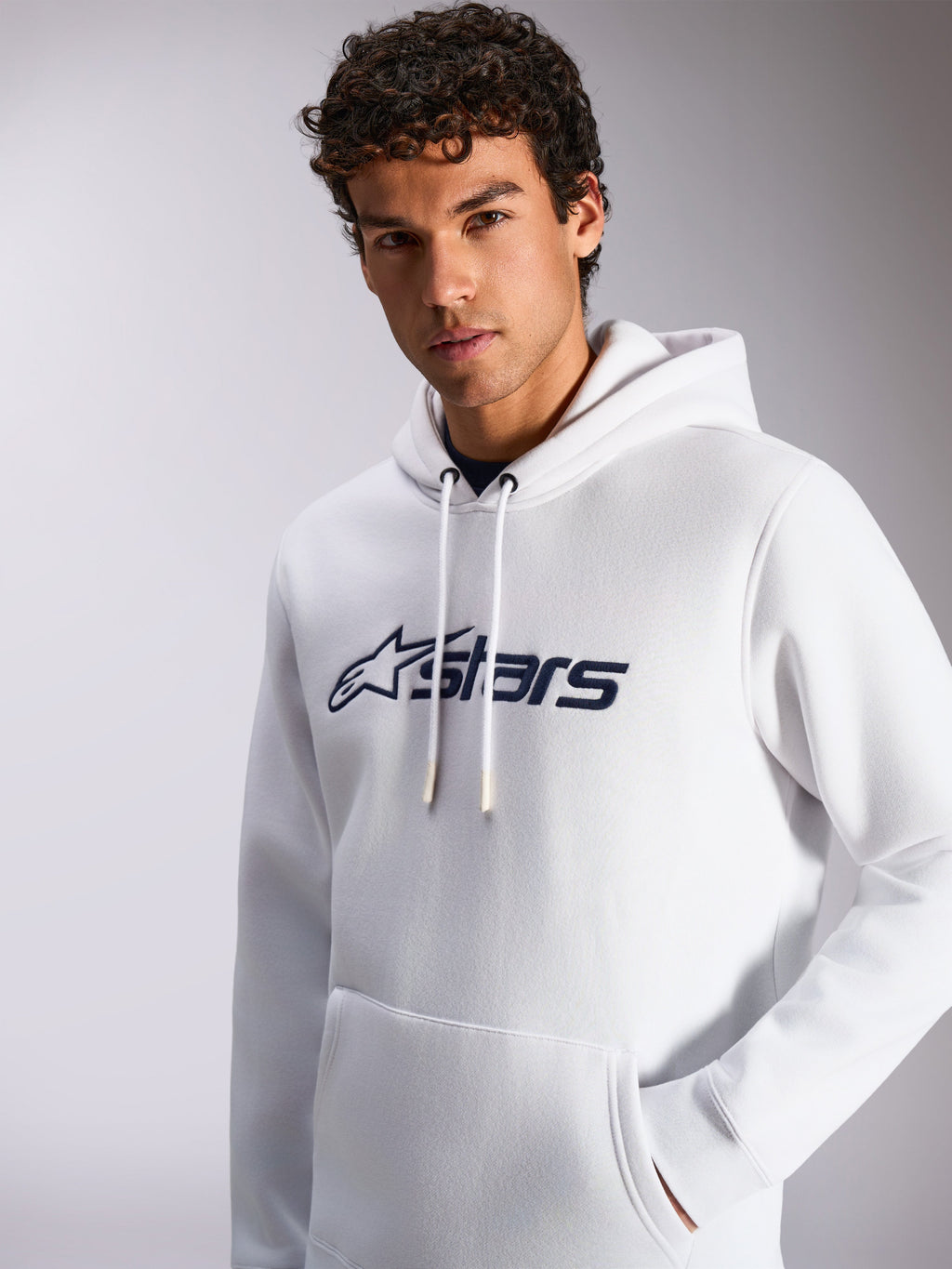 Felpa con cappuccio Alpinestars Blaze V3, bianco e blu navy, indossata da un modello, abbigliamento sportivo casual, logo Alpinestars blu navy sul davanti, cappuccio con cordoncino, tasca a marsupio, design lifestyle moderno