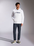 Alpinestars Blaze V3 Hoodie, felpa casual streetwear bianca con logo Alpinestars blu navy sul petto, indossata da un modello con jeans blu scuro e sneakers color sabbia, con cappuccio con coulisse e tasca a marsupio frontale