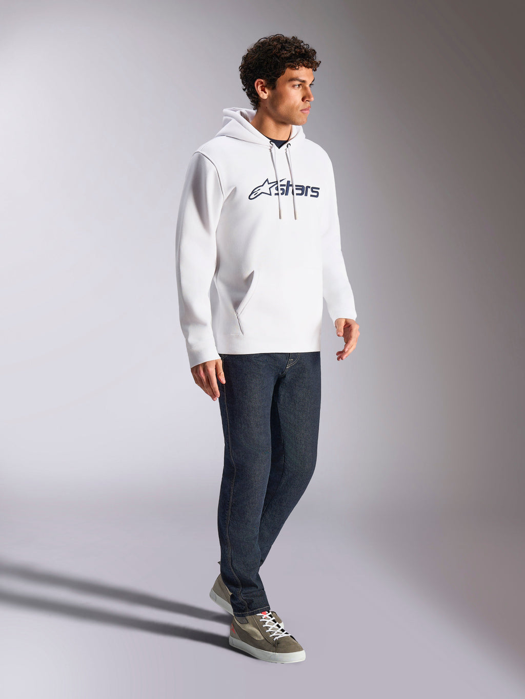 Felpa con cappuccio Alpinestars Blaze V3, bianco e navy, streetwear casual indossato da un modello con jeans blu scuro e sneakers, dotata di cappuccio con cordoncino e stampa del logo audace sul davanti, design moderno ispirato al motorsport