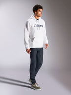 Felpa con cappuccio Alpinestars Blaze V3, bianco e navy, streetwear casual indossato da un modello con jeans blu scuro e sneakers, dotata di cappuccio con cordoncino e stampa del logo audace sul davanti, design moderno ispirato al motorsport
