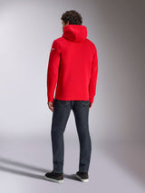 Felpa con cappuccio Alpinestars Linear Wordmark V3, felpa casual rossa, vista posteriore con cappuccio e logo Ageless bianco sulla manica, abbinata a jeans blu scuro e scarpe nere, lifestyle motorsport streetwear