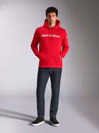 Felpa con cappuccio Alpinestars Linear Wordmark V3, streetwear casual, rossa con scritta lineare bianca sul petto, cappuccio con cordino, tasca a marsupio frontale, indossata con jeans scuri e sneakers nere, design moderno ispirato al motorsport