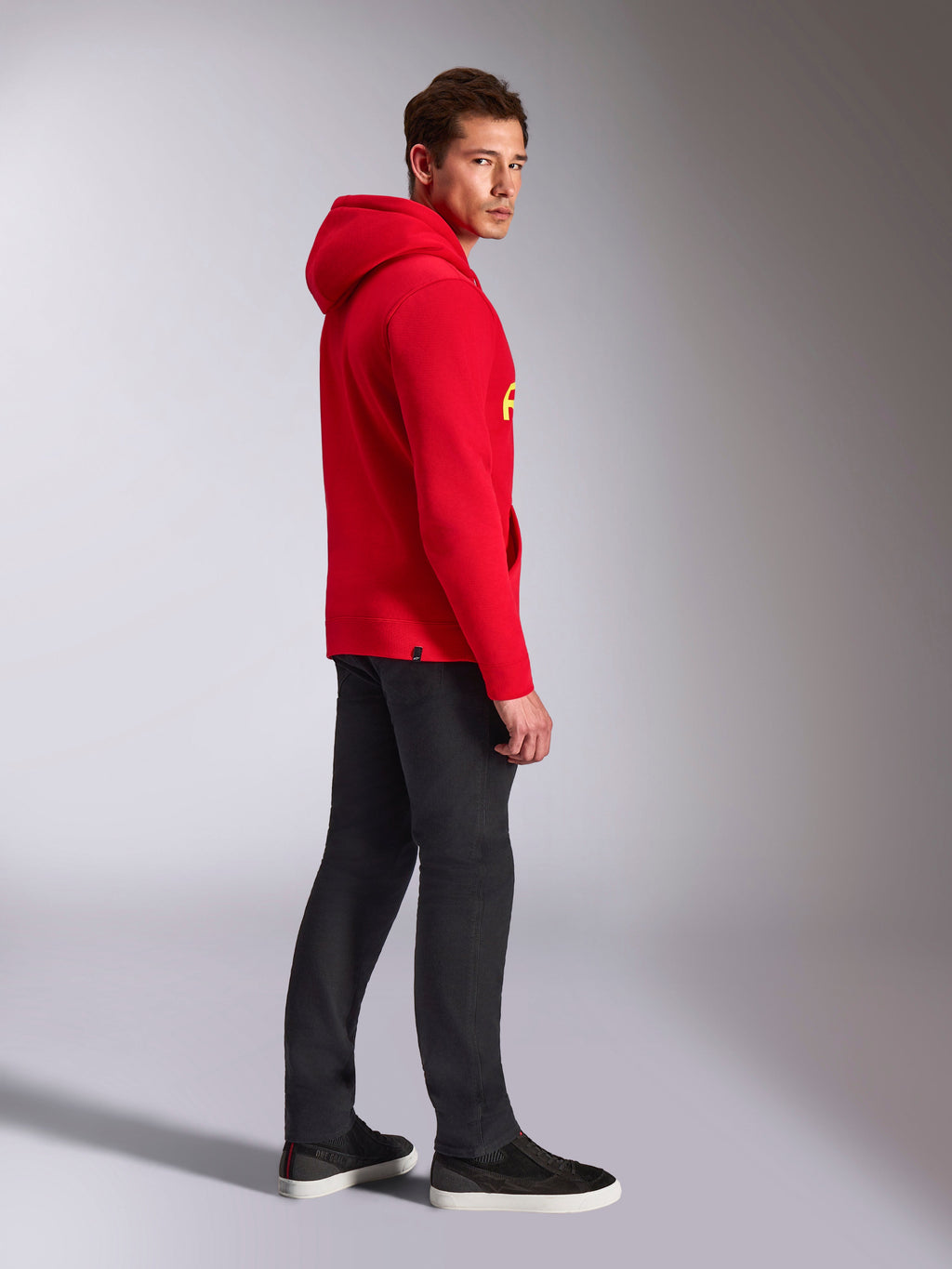 Alpinestars Ride V3 Hoodie, abbigliamento sportivo casual, rosso con marchio giallo alta visibilità, modello che indossa la felpa rossa con pantaloni neri e sneaker, vista di profilo, design pullover in pile con polsini e orlo a coste.
