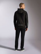 Felpa con cappuccio Alpinestars Sessions V3, streetwear casual, nera con scritta Alpinestars grigia sulla parte inferiore della schiena e marchio 'astars' sulle maniche, vista posteriore di un modello maschile che indossa la felpa e pantaloni neri, design moderno ispirato al motorsport