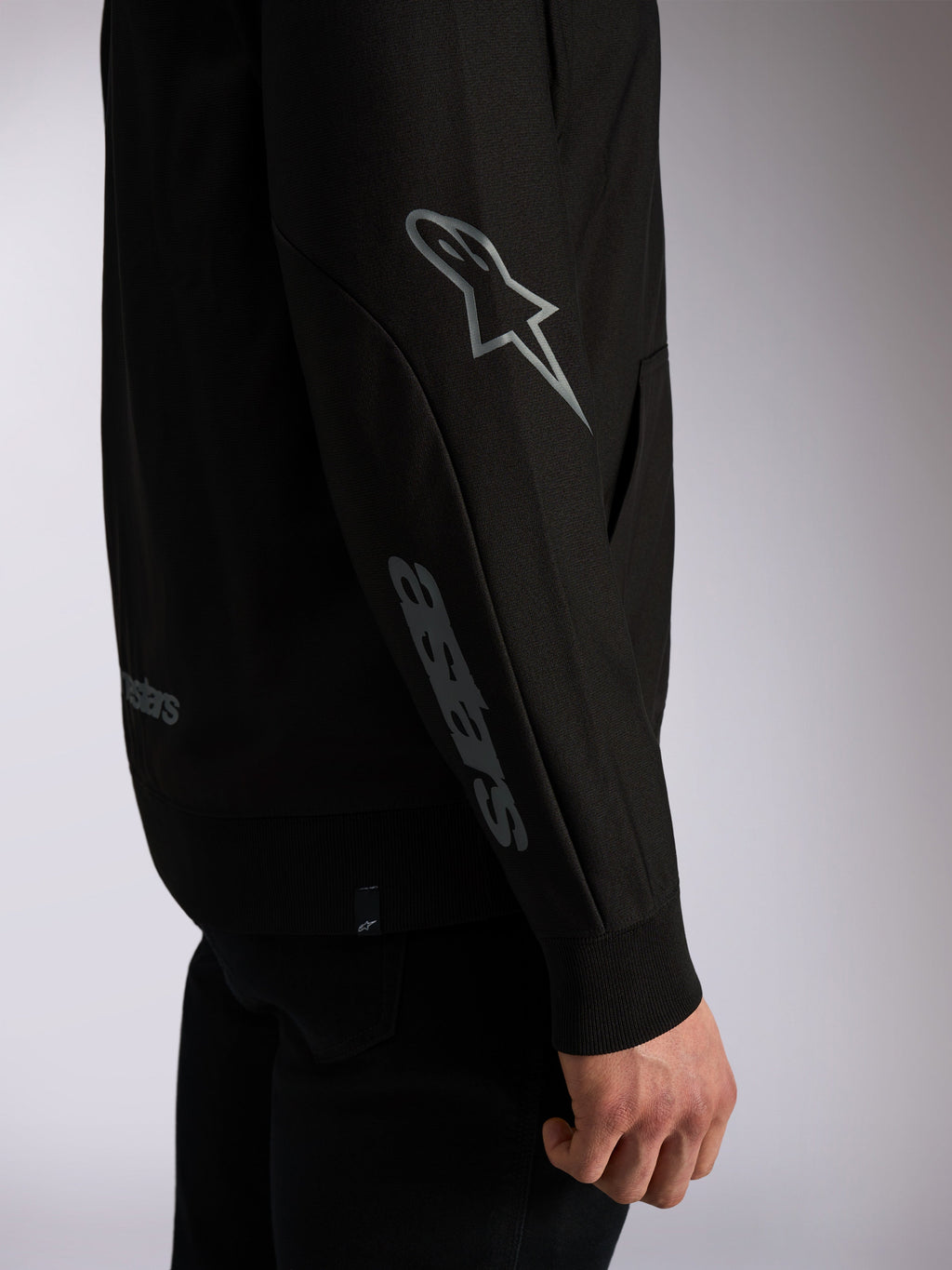 Alpinestars Sessions V3 Hoodie, felpa streetwear casual nera, primo piano della manica con logo Astars grigio sul gomito e scritta sull'avambraccio, polsini a coste, design ispirato al motorsport
