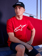 Cappello Profile Alpinestars nero, scatto lifestyle di un uomo che indossa il cappello con visiera curva e una t-shirt rossa con logo Alpinestars bianco, streetwear casual ispirato al motorsport