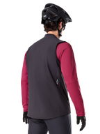Gilet Termico Alpinestars A-Dura, nero, vista posteriore, indossato sopra una maglia a maniche lunghe bordeaux con casco da mountain bike e guanti neri, abbigliamento da ciclismo isolante leggero per il fuoristrada