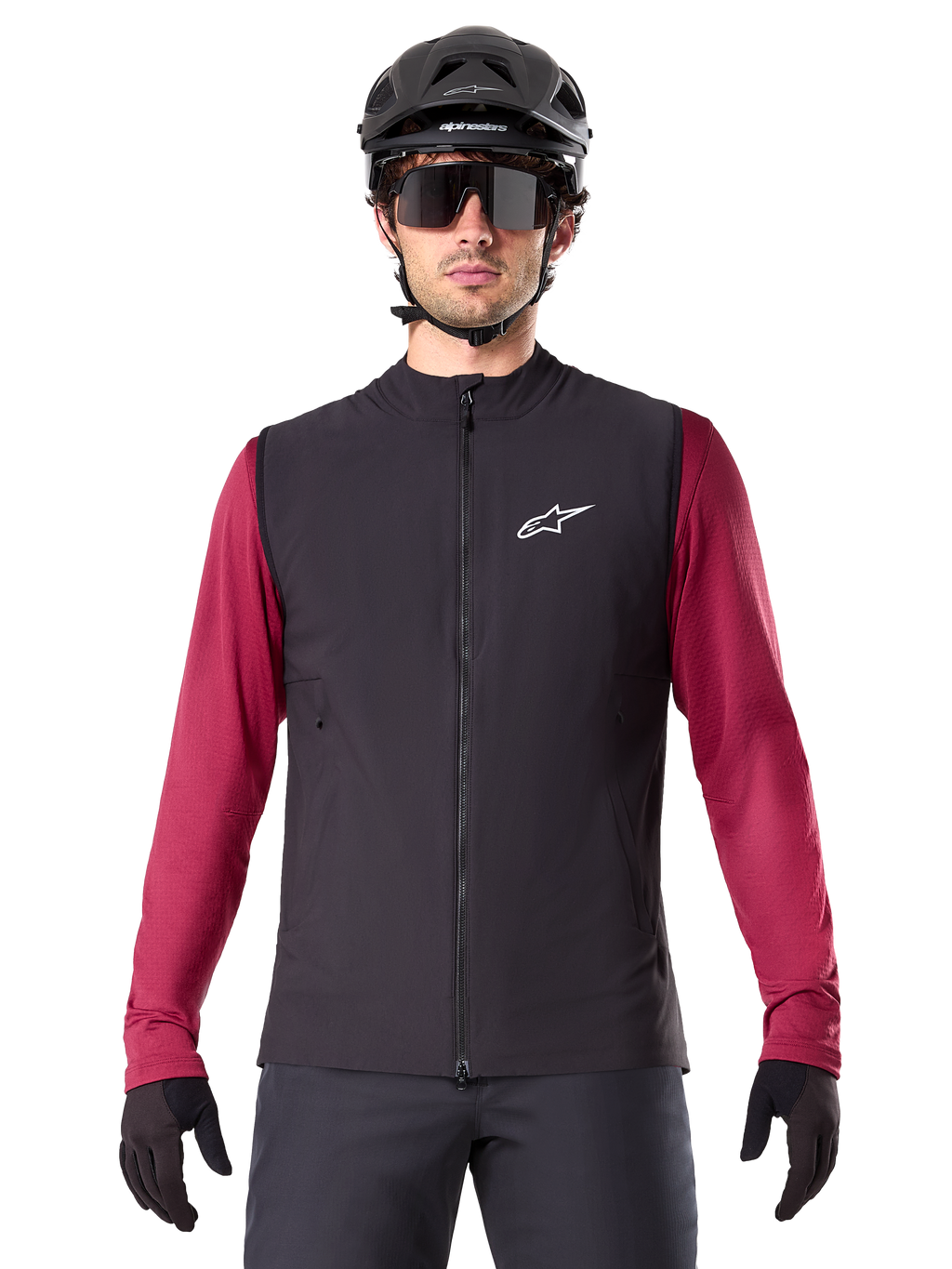 Gilet termico Alpinestars A-Dura, gilet da ciclismo isolato nero, indossato da un modello con maglia bordeaux a maniche lunghe, casco da MTB nero e occhiali da sole, con logo bianco sul petto, protezione termica leggera per mountain bike