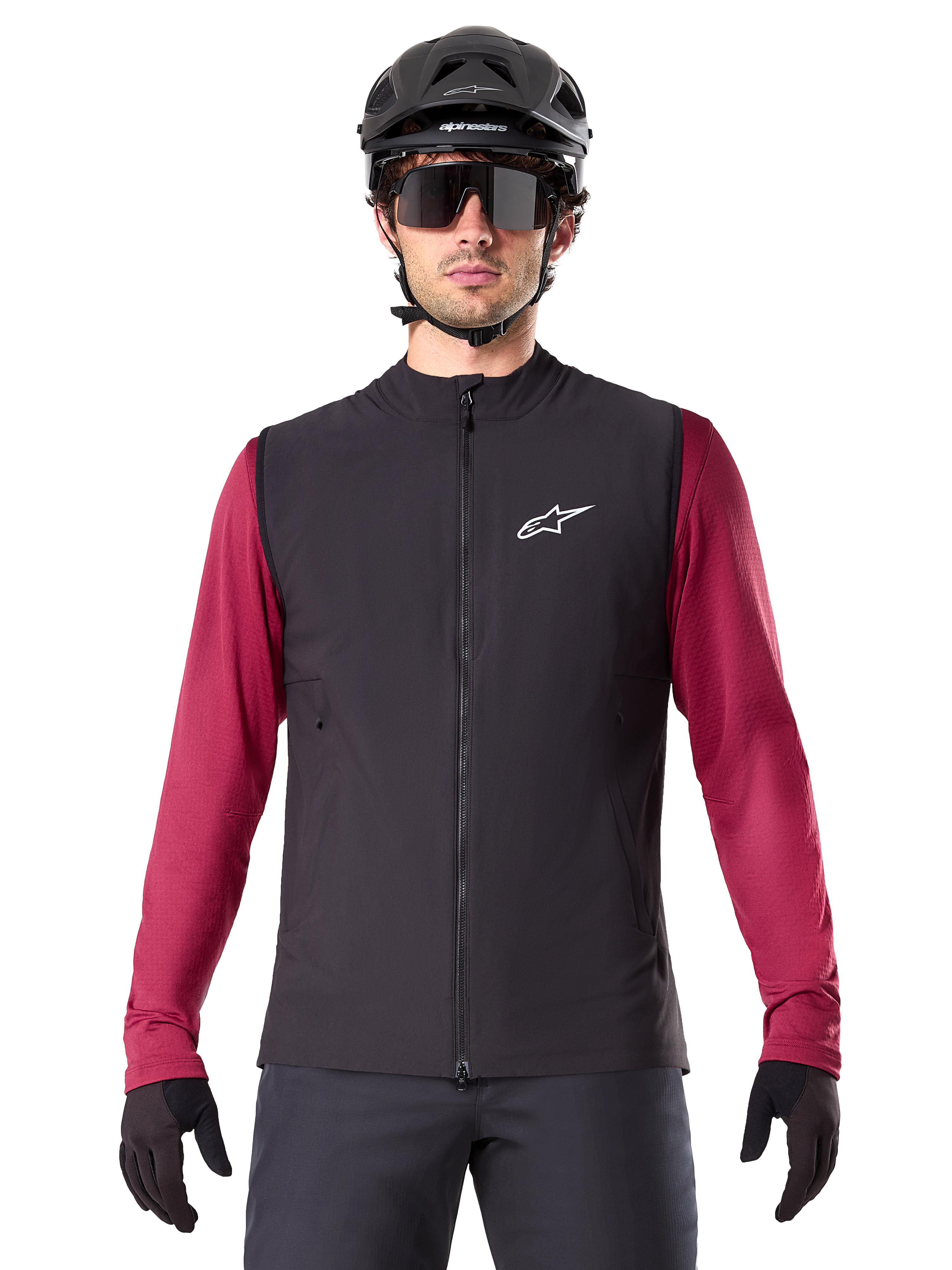 Gilet termico Alpinestars A-Dura, gilet da ciclismo isolato nero, indossato da un modello con maglia bordeaux a maniche lunghe, casco da MTB nero e occhiali da sole, con logo bianco sul petto, protezione termica leggera per mountain bike