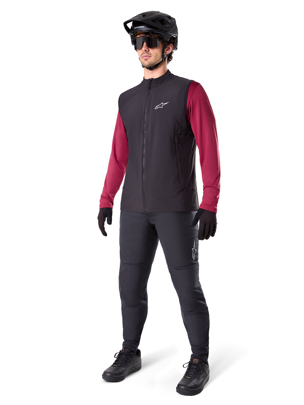 Gilet Termico Alpinestars A-Dura, gilet da ciclismo nero, indossato da un rider sopra una maglia a maniche lunghe bordeaux e pantaloni neri, con casco da MTB e guanti neri, progettato per il mountain biking in climi freddi