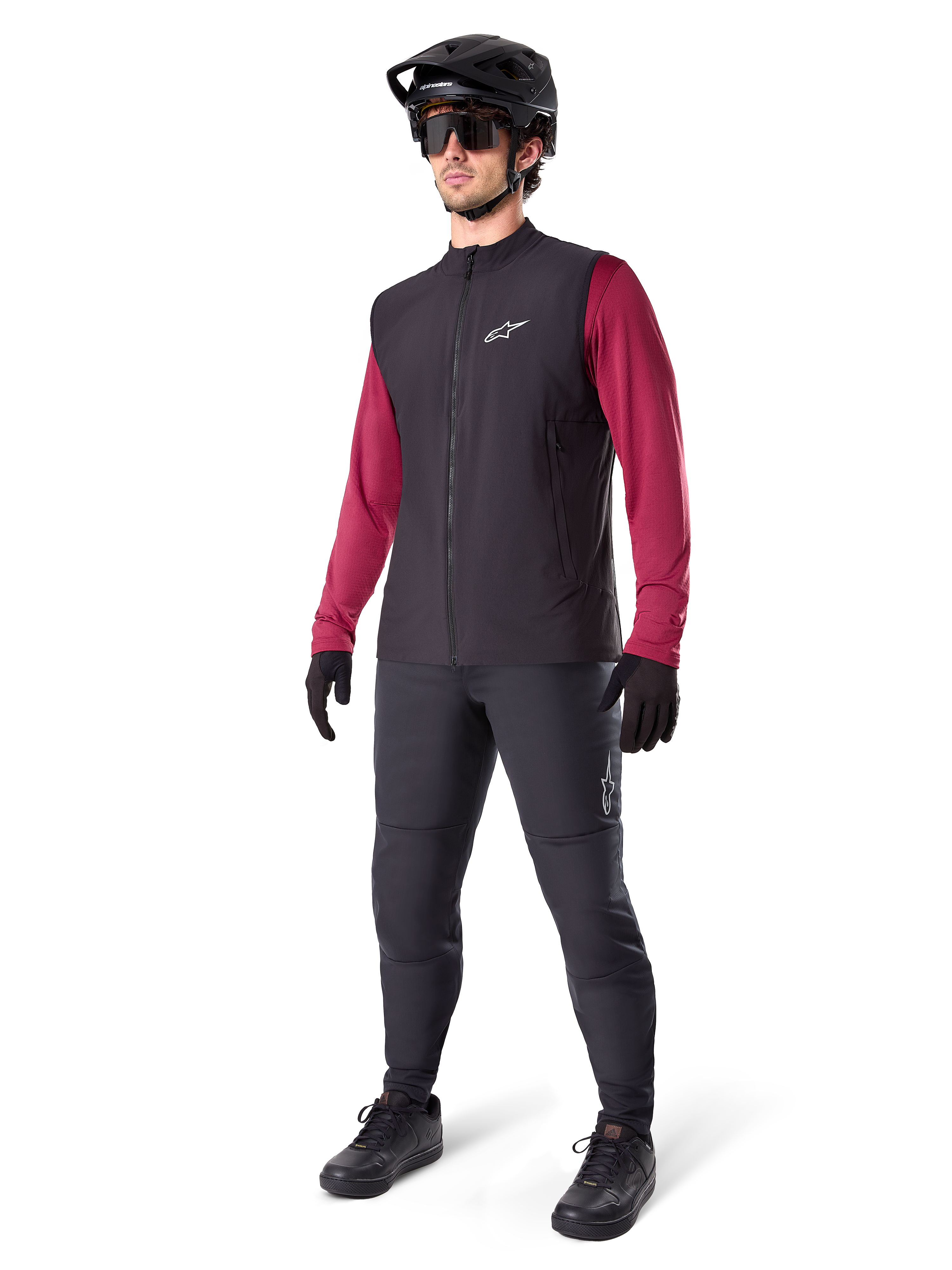 Gilet Termico Alpinestars A-Dura, gilet da ciclismo nero, indossato da un rider sopra una maglia a maniche lunghe bordeaux e pantaloni neri, con casco da MTB e guanti neri, progettato per il mountain biking in climi freddi